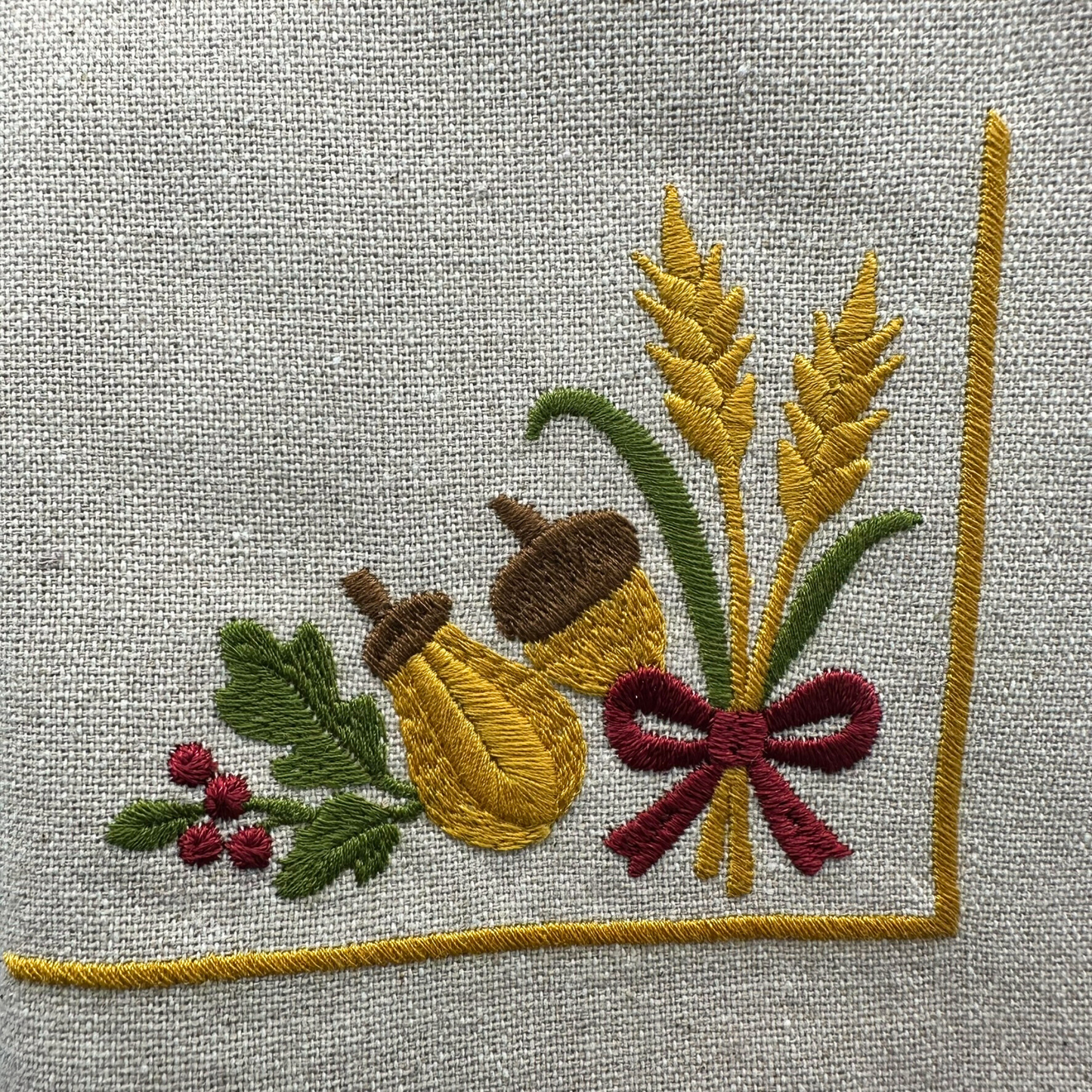 Embroidered design of oak leaves, acorns, and wheat, ribbon on napkin