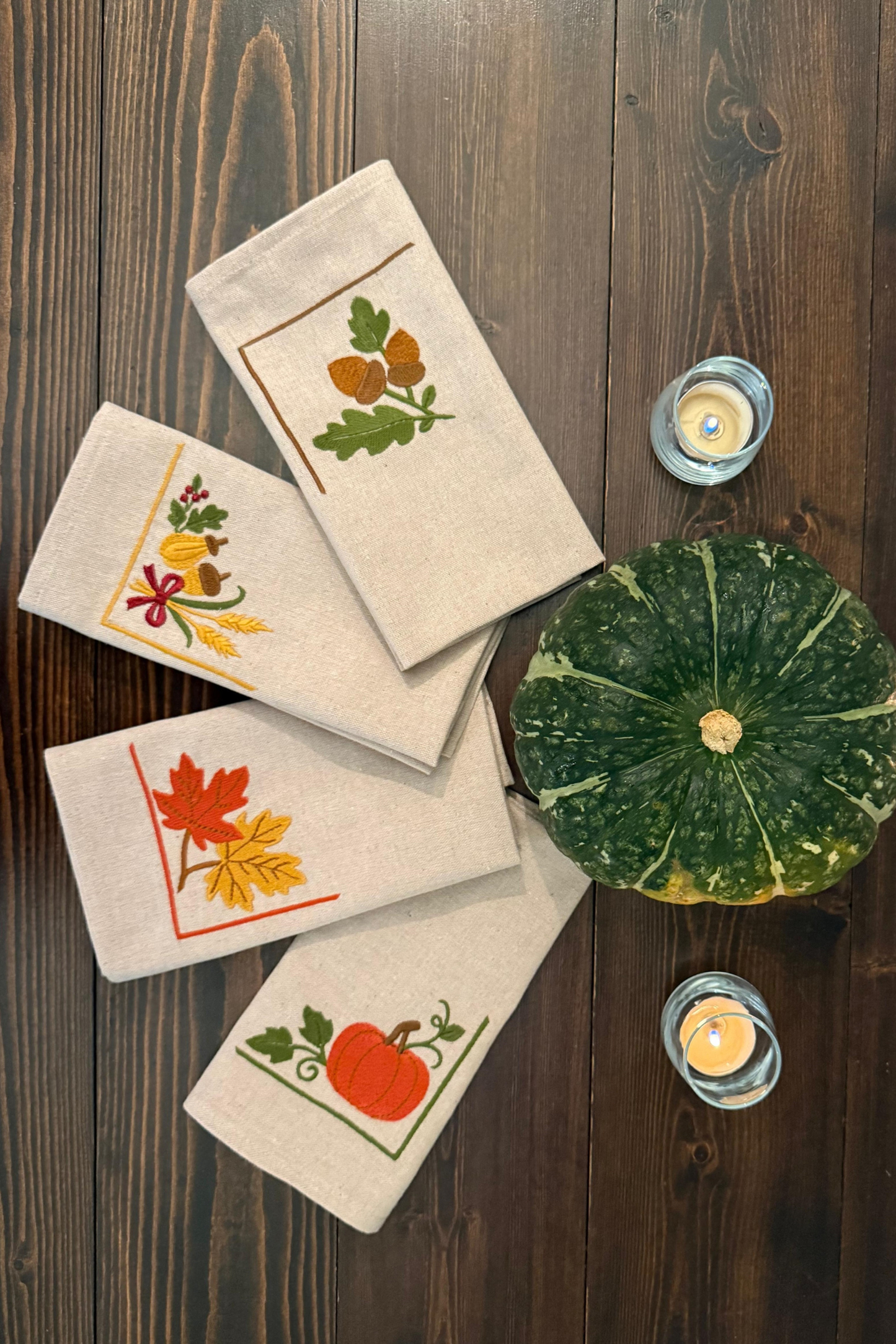 Folded cloth napkins featuring acorns, harvest motifs, leaves and pumpkin embroidery.