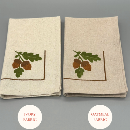 Two folded napkins with embroidered acorn and leaf design 