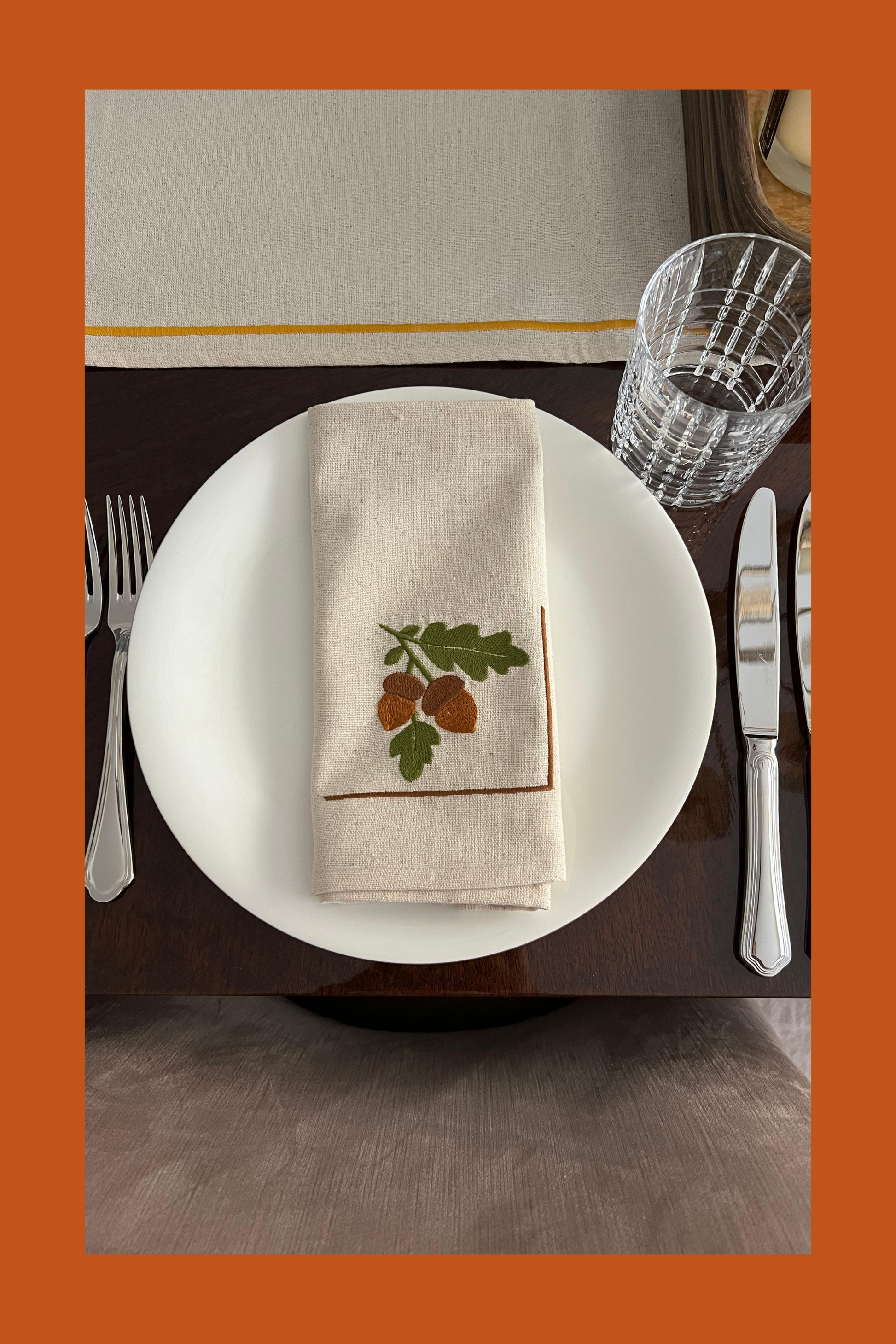 Table setting with an embroidered napkin featuring oak leaf and acorn design.