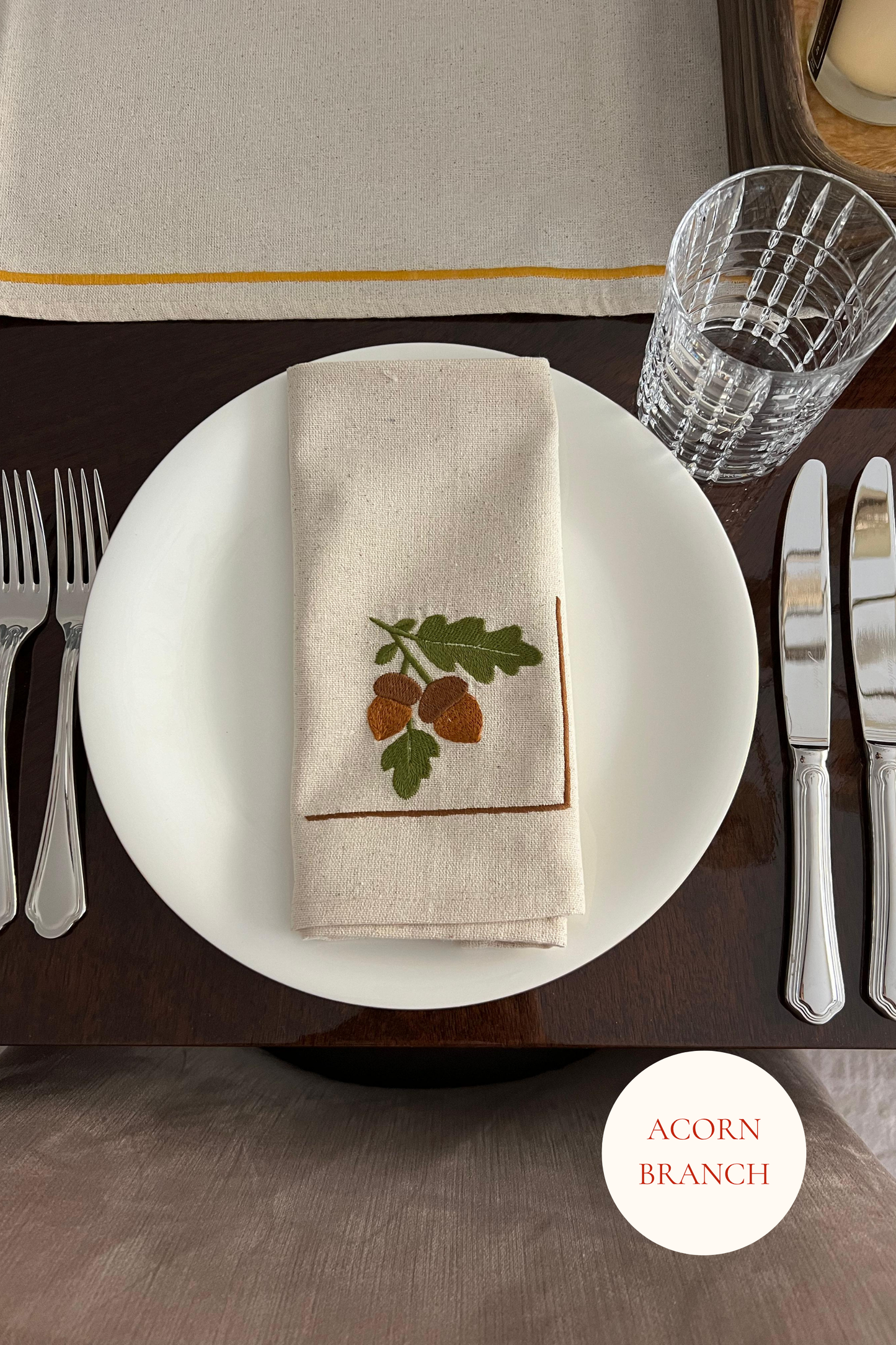 Dining table setting with a embroidered napkin featuring acorns and oak leaves.