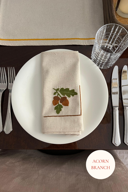 Dining table setting with a embroidered napkin featuring acorns and oak leaves.