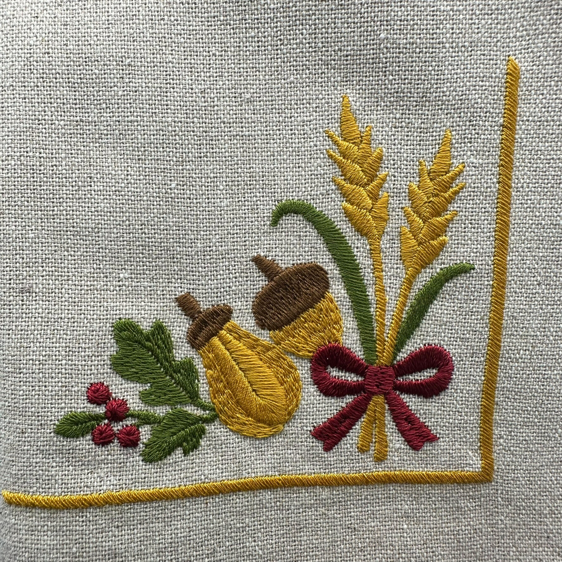 Embroidered design of oak leaves, acorns, and wheat, ribbon on napkin