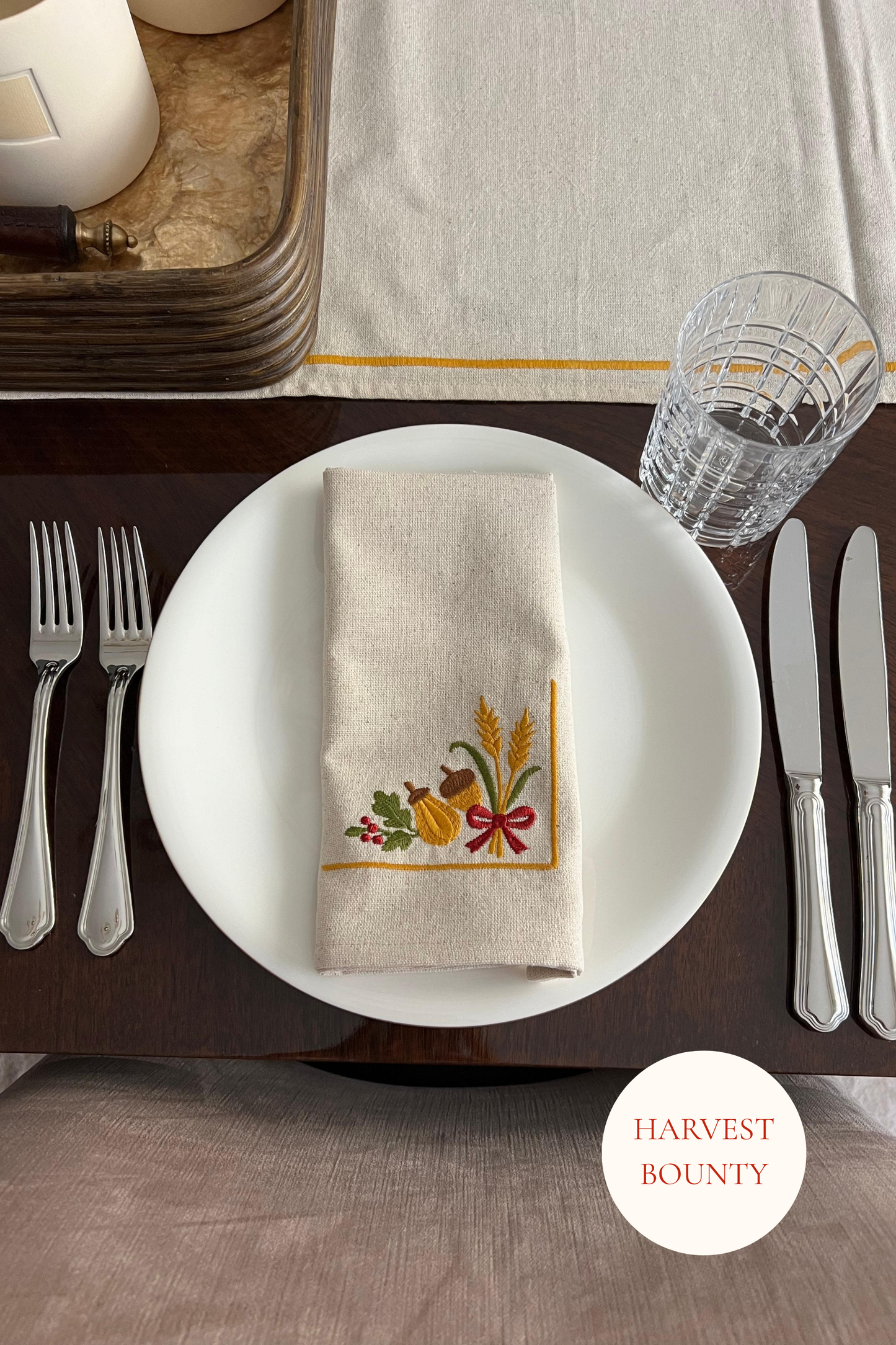 Dining table setting with a embroidered napkin featuring harvest-themed design.