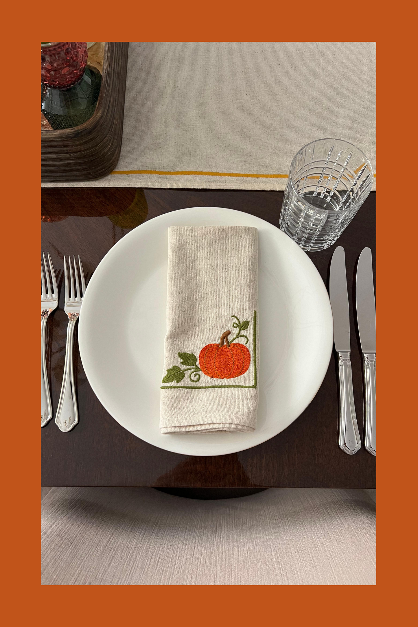Table setting with an embroidered napkin featuring pumpkin design.
