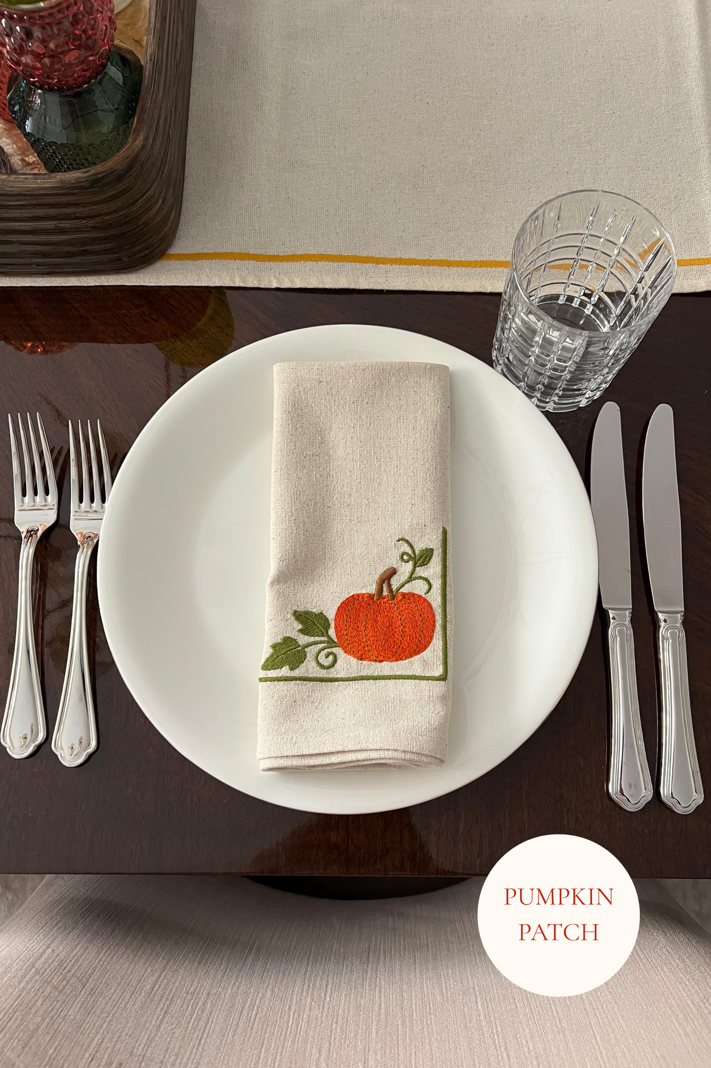 Dining table setting with embroidered pumpkin-themed napkin on a white plate.