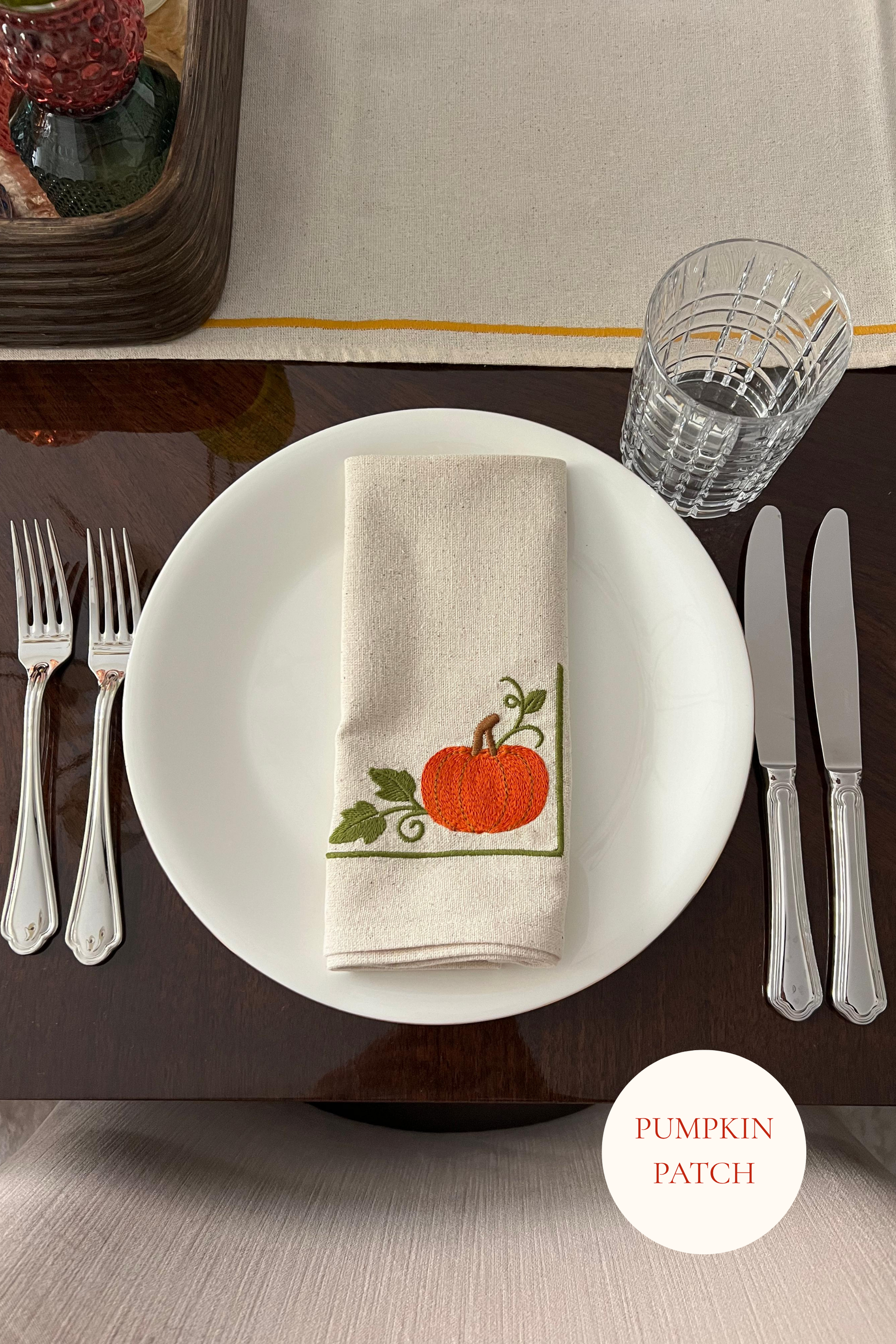 Dining table setting with embroidered pumpkin-themed napkin on a white plate.