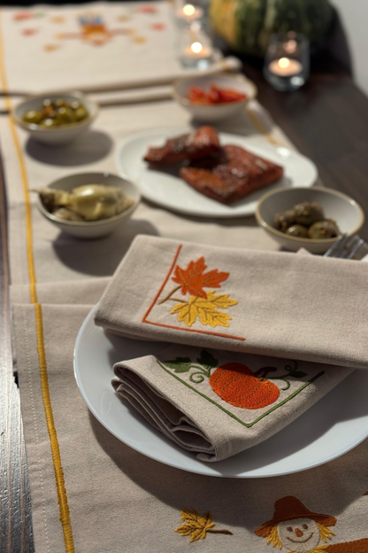 Table setting with embroidered napkins featuring leaves and pumpkins on a table.