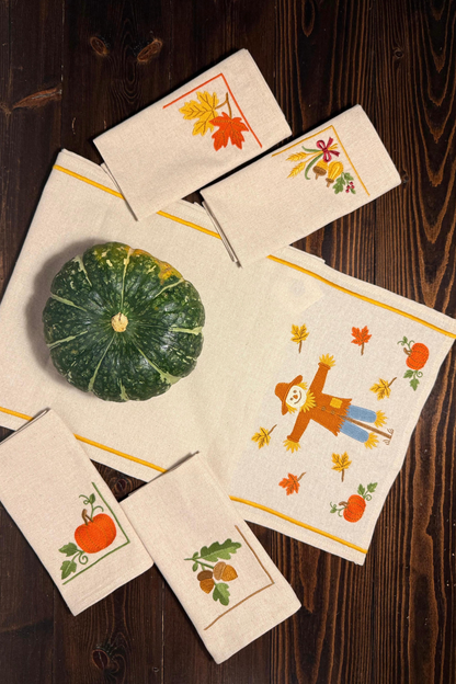 Set of dinner napkins and table runner with autumn-themed designs on a wooden surface