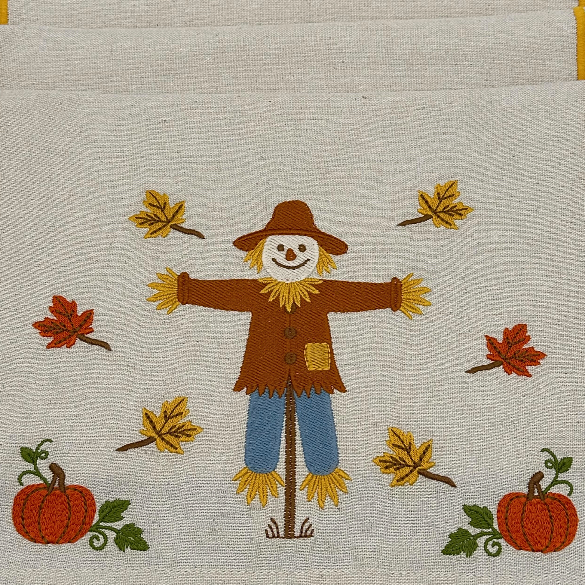 Embroidered design of a scarecrow with pumpkins and leaves on fabric.