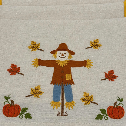 Embroidered design of a scarecrow with pumpkins and leaves on fabric.