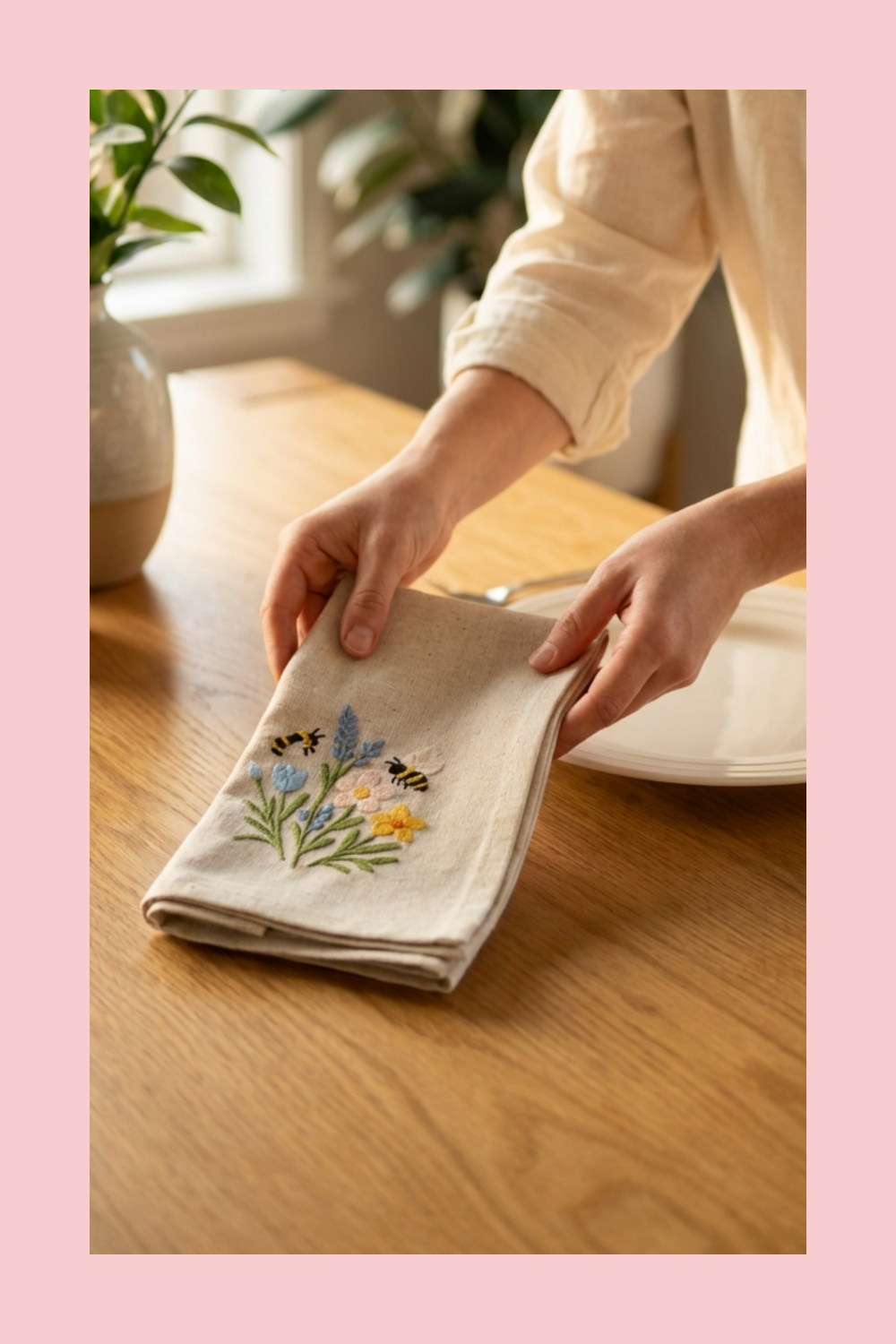 Person holding a folded napkin with floral embroidery on a wooden table.