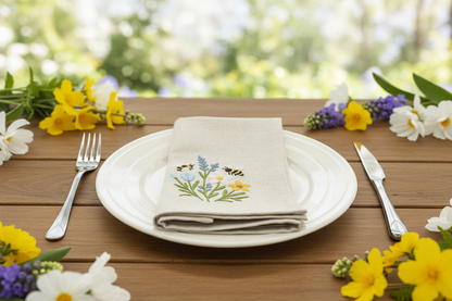 Table setting with embroidered napkin featuring floral and bee design on a wooden table with flowers.