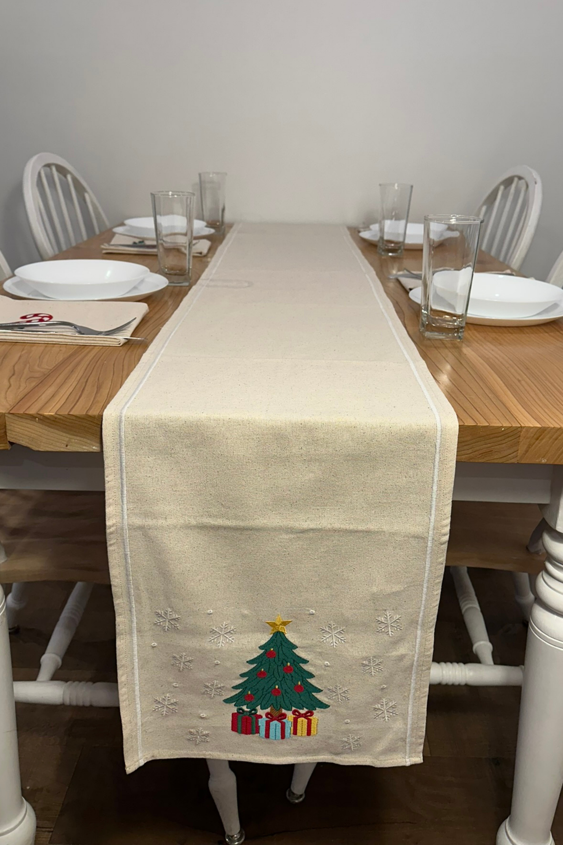 Dining table set with a Christmas-themed embroidered table runner featuring a tree and presents.